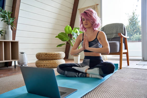Young calm woman pink hair meditate watching online yoga class tutorial at home. Young healthy woman pink hair wears sportswear meditating watching online class tutorial on laptop at home. Fit sporty teen girl doing yoga training fitness workout sport exercise feels stress free. teen yoga stock pictures, royalty-free photos & images