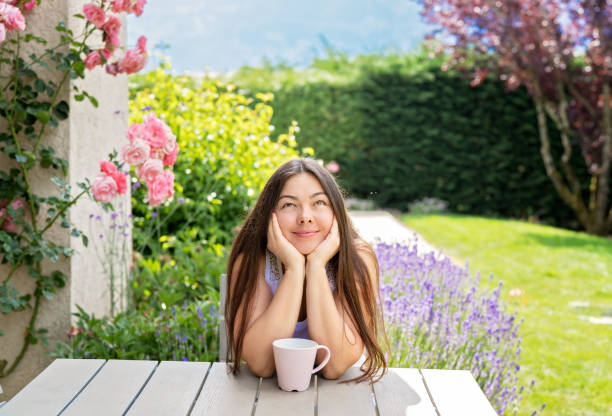 beautiful 40 years old woman sitting on terrace in blooming summer garden daydreaming enjoying tea. young girl with long hair spending vacatiopn at countryside. natural beauty - 35 40 years fotos imagens e fotografias de stock