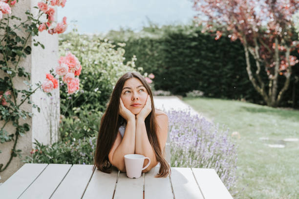 hermosa mujer de 40 años sentado en la terraza en flor en el jardín de verano en flor soñando disfrutando del té. joven con pelo largo pasando las vacaciones en el campo. belleza natural - 35 40 years fotografías e imágenes de stock