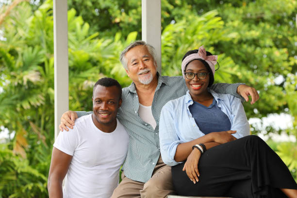 Portrait of senior Asian uncle with young couple of black African American who live happily and peacefully in the same green neighborhood Portrait of senior Asian uncle with young couple of black African American who live happily and peacefully in the same green environment neighborhood godfather godparent stock pictures, royalty-free photos & images