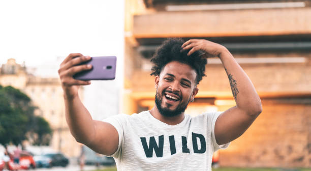 Vain man taking a selfie outdoors Smart phone, Mobile phone, Selfie, Self portrait, Afro man, Hair style graphic t shirt stock pictures, royalty-free photos & images