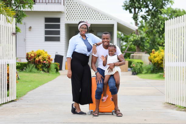 la famiglia afroamericana si trasferisce in una nuova casa con il padre che tiene il bambino con valigia e bagaglio con il sorriso - child caribbean black latin american and hispanic ethnicity foto e immagini stock