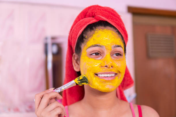 Beautiful girl applying yellow turmeric face pack on face.