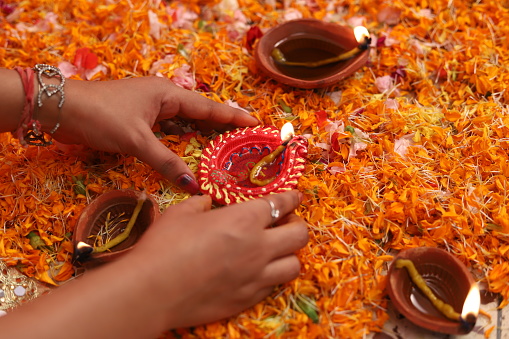 Close up of women hand holding Diwali lamp or Diya , Decorated with colorful flowers.