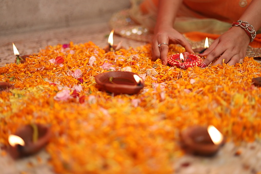 Close up of women hand holding Diwali lamp or Diya , Decorated with colorful flowers.