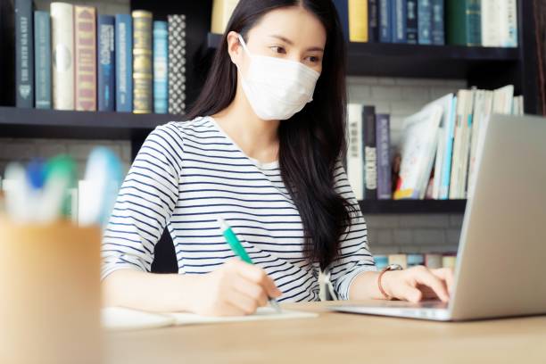 istock Woman wearing surgical mask working with laptop computer in library. 1269125425