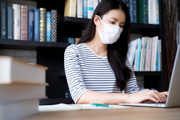 istock Woman wearing face mask working with laptop in library 1269125429