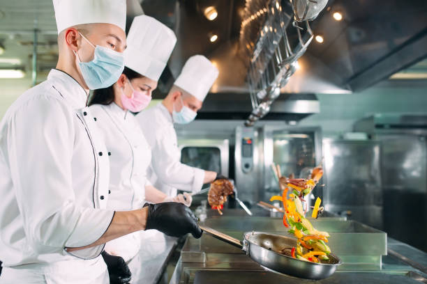 Chefs in protective masks and gloves prepare food in the kitchen of a restaurant or hotel. stock photo