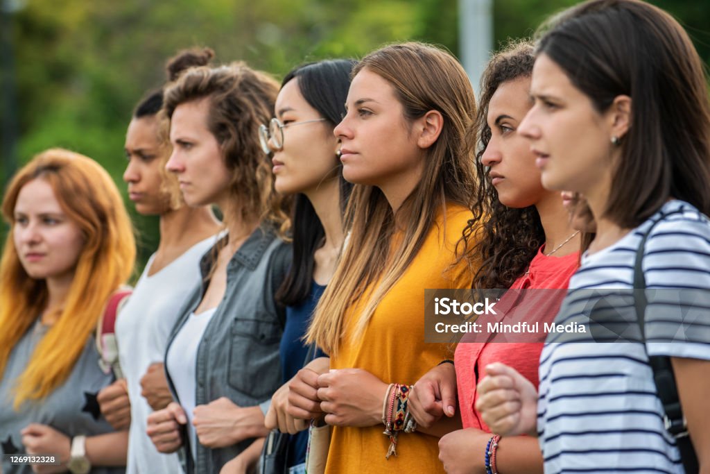 Women standing together Group of young female protestors with arms in arms and clenching fist while standing together outdoors Women's Rights Stock Photo