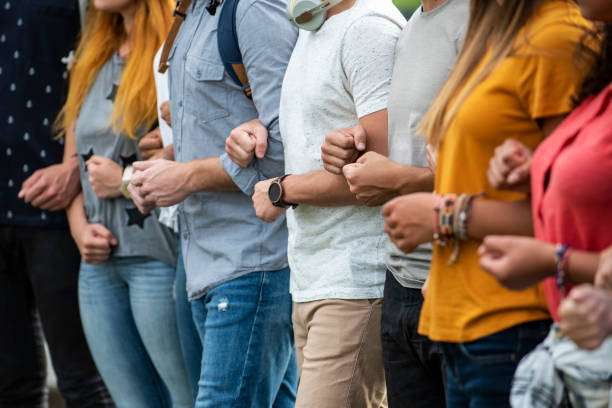 Protestors standing together Group of young male and female protestors with arms in arms and clenching fist while standing together outdoors anti racism photos stock pictures, royalty-free photos & images