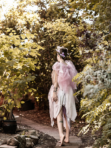 Portrait of young woman dressed as fairy. Exterior of beautiful back yard garden.