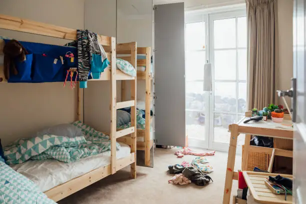 Wide shot of a messy child's bedroom with bunk beds and there are clothes on the floor.