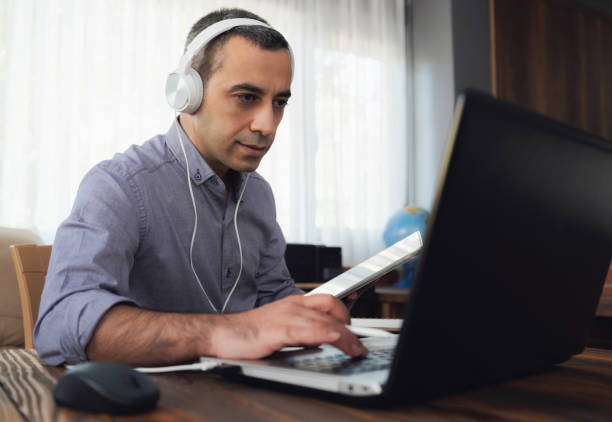 istock Man Is Working Online In Home Office Using His Laptop Computer, Joining Webinar And Taking Notes On Digital Tablet 1269142491