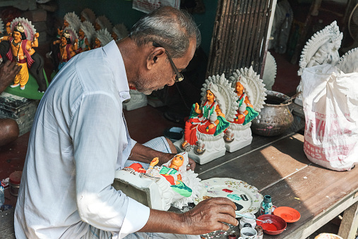 Kumortuli, Kolkata, 9/14/2019: Few days before Laxmi puja, an artisan is painting clay idols of Goddess Laxmi inside his workplace. He is holding a paintbrush & a colour palette is placed in front.