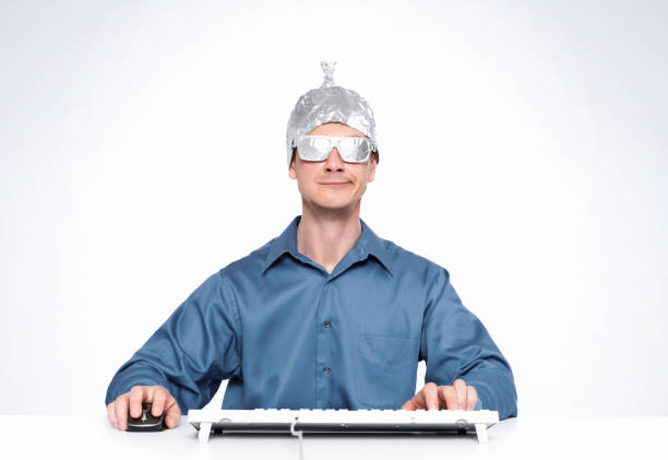 Conceptual Man with an aluminum foil hat and aluminum glasses behind a keyboard in front of a computer. Conceptual Man with an aluminum foil hat and aluminum glasses behind a keyboard in front of a computer. tin foil hat stock pictures, royalty-free photos & images