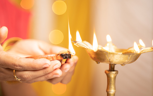 Closeup of woman hands lighting lantern diya or Lamp during festival ceremony - concept of traditional Indian festival and ritual celebrations