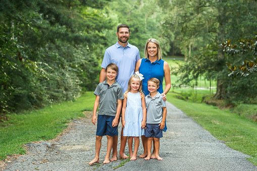 Family of five portrait outdoors on a summer day on a country road with trees surrounding them