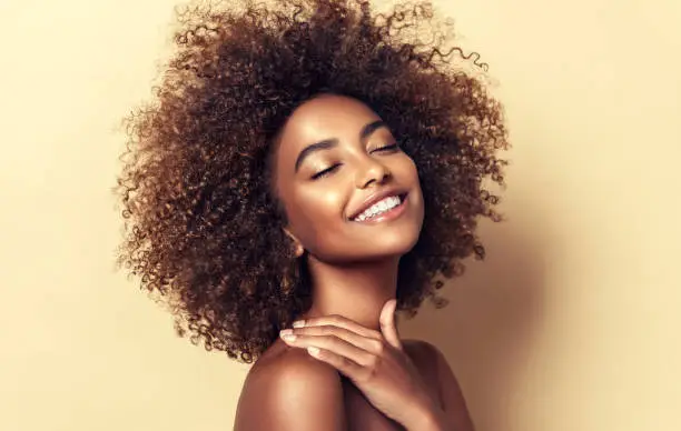 Photo of Natural Afro hair. Wide toothy smile and expression of pleasure on the face of young brown skinned woman. Afro beauty.