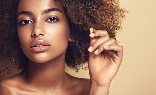 Close-up portrait of young brown skinned young woman with thoughtful and sincere look at viewer. Girl with vibrant, melanin-rich skin tone and natural Afro hairstyle. Beauty of youth.