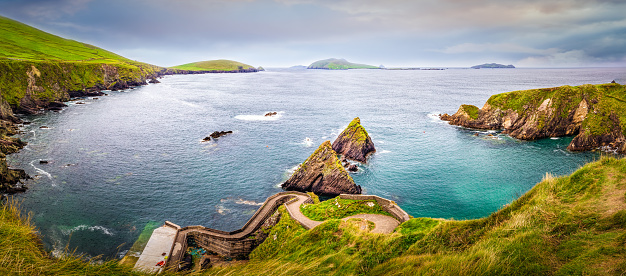 Beautiful view on Dunquin Harbour and small rocky islands with turquoise water and green fields in the background. Dingle peninsula, Co Kerry, Ireland