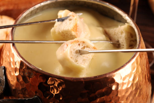 istock Gourmet Swiss fondue dinner on a winter evening with assorted cheeses on a board alongside a heated pot of cheese fondue with two forks dipping 1269162402