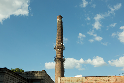 Red brick stack of the old chimney on the large abandoned mill, clear blue sky in the morning.