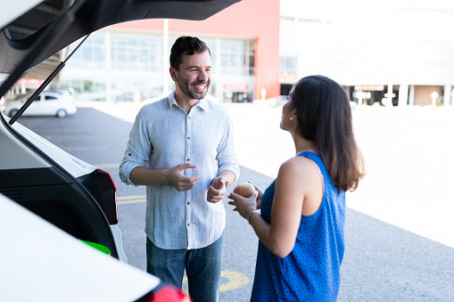 Couple Talking While Standing By Car At Parking Lot