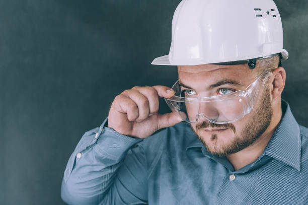 istock A man in safety glasses and a construction helmet on a dark background. 1269174670