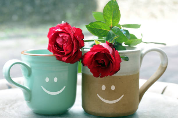 Couple cup of tea or coffee with happy smiling face symbol on it and two red roses. Valentines Day, togetherness and an healthy relationship concept.