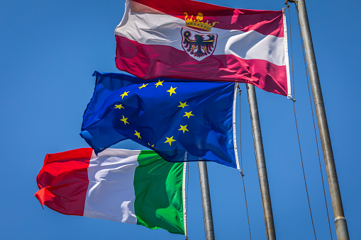 Flags pattern: Italian, Austrian and Euro flags waving in the sky