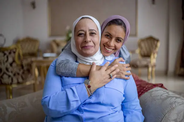 Muslim senior mother and her adult daughter hugging in the living room.