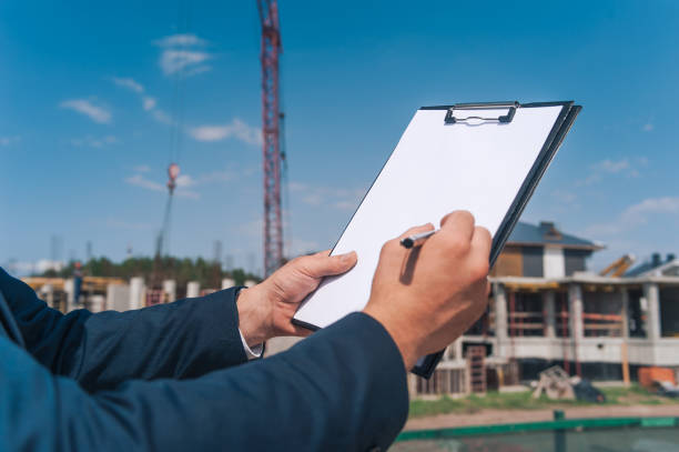 istock The chief in a jacket and a construction helmet with documents in his hands, against the background of a tower crane and the sky with clouds. House construction inspection. 1269222516