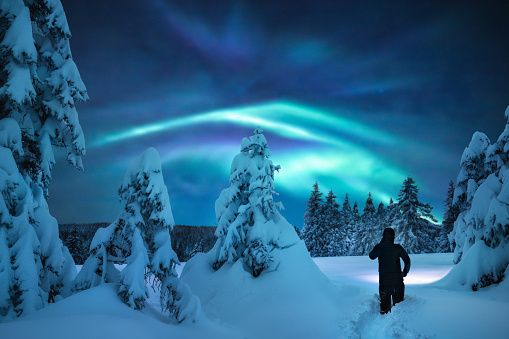 Man hiking in knee-deep snow under the beautiful night sky with colorful aurora borealis.