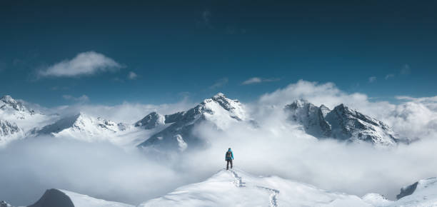 Mountain Hiker Man standing on the top of a snowcapped mountain peak. Panoramic view. mountain peak stock pictures, royalty-free photos & images