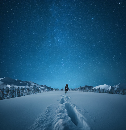 Woman walking in knee-deep snow under the starry night sky.
