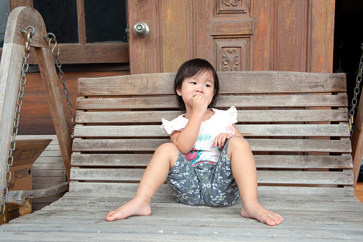 A asian young girl sitting on a swing enjoying with an apple slice in hand