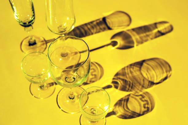 Wine glasses on a sunny table cast shadows, sunlight, crystal glassware, wine glasses, champagne flute on yellow background.