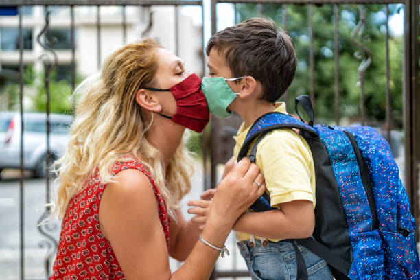 istock Little boy with a backpack on his back kissing his mom with protective masks  and going back to school, during COVID-19 1269245656