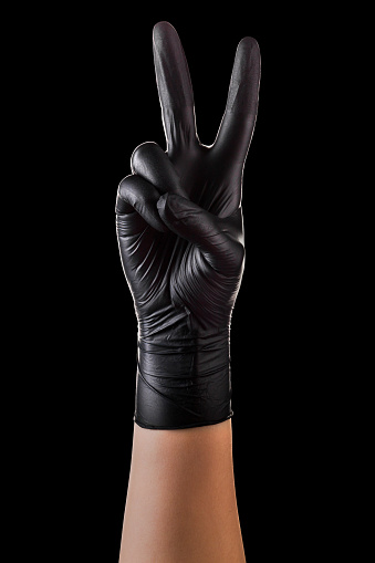 Hand in black gloves showing two fingers up in the peace or victory symbol isolated on black background. Isolated with clipping path.