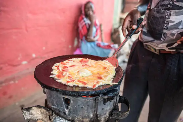 Jinja, Uganda - September 30, 2016: Man cooking omelette with tomato and onion, local dish called rolex