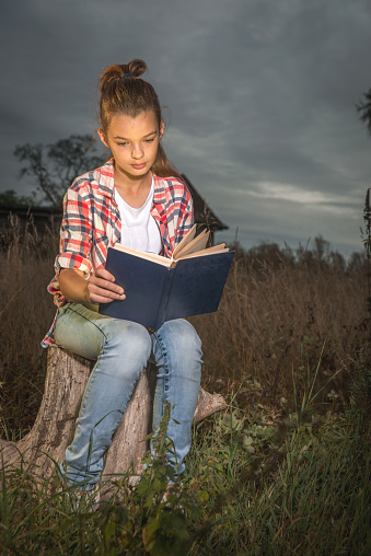 A girl reads a book in the evening twilight.