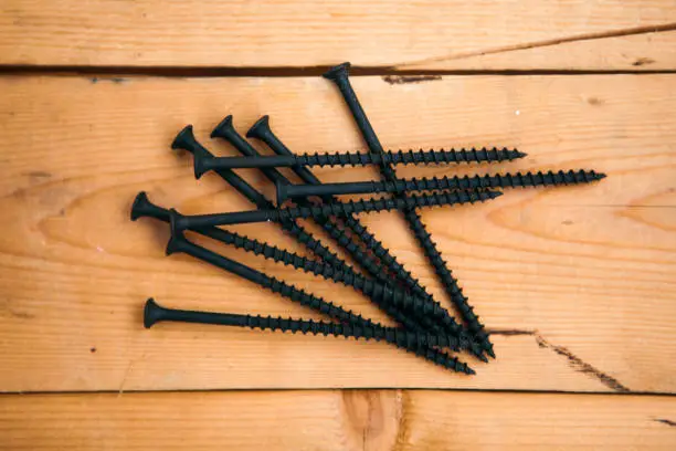 Photo of Set of old black drywall screws on the wooden background