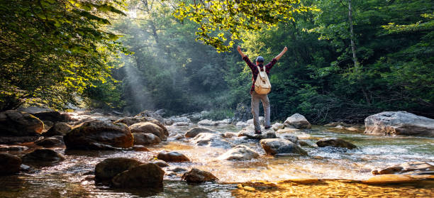 川の近くの森の屋外でトレッキング幸せな男性ハイカー - river crossing ストックフォトと画像