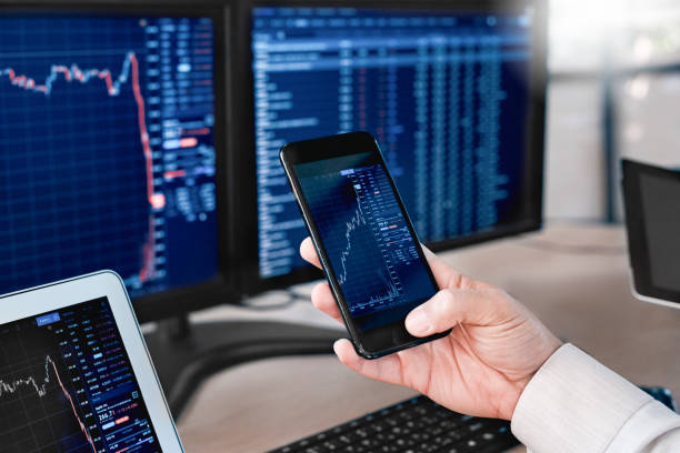 istock Stocks and Funds. Trader sitting at office in front of monitors with data using app on smartphone monitoring price changes close-up 1269256849