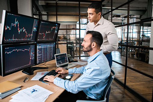 Two successful trader in formalwear working together in office, looking at screen, checking global currency index on fund exchange