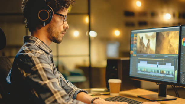 istock Evening in Creative Office: Professional Videographer / Audio Engineer Wearing Headphones Works on Desktop Computer, Screen Shows: Footage Montage, Using Video Editing Software, Syncing Audio Track 1269257021