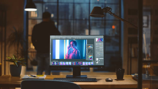 現代クリエイティブオフィスの机の上に立っている写真編集ソフトウェアを持つデスクトップコンピュータ。カップからのバックグラウンドデザイナードリンクでは、窓の外のナイトシティ� - colorist ストックフォトと画像