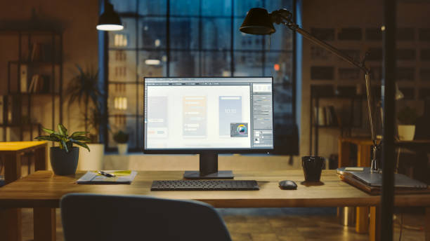 istock Shot of a Desktop Computer in the Office Shows Screen with Mobile Phone Application Design, Software UI Development. In the Background Warm Evening Lighting and Open Space Studio with City Window View 1269257066