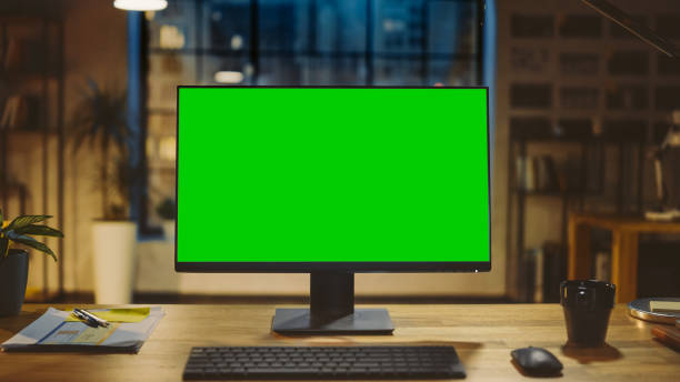 istock Desktop Computer with Mock-up Green Screen Standing on the Wooden Desk in the Modern Creative Office. In the Background Warm Evening Lighting and Open Space Studio with City Window View. 1269257077