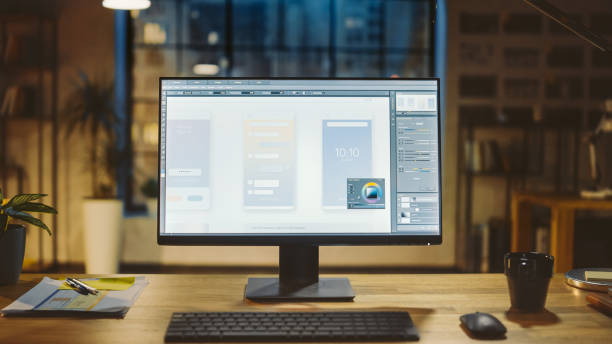 istock Shot of a Desktop Computer in the Office Shows Screen with Mobile Phone Application Design, Software UI Development. In the Background Warm Evening Lighting and Open Space Studio with City Window View 1269257122